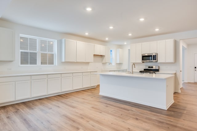 kitchen with a kitchen island with sink, light wood-type flooring, white cabinets, and appliances with stainless steel finishes