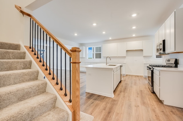 kitchen with sink, white cabinetry, light wood-type flooring, appliances with stainless steel finishes, and a kitchen island with sink