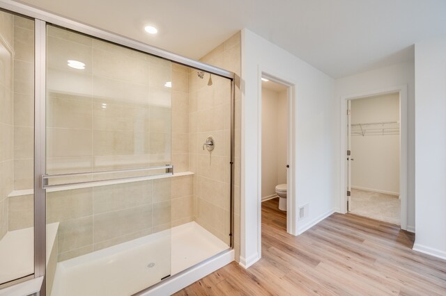 bathroom with hardwood / wood-style flooring, toilet, and a shower with shower door