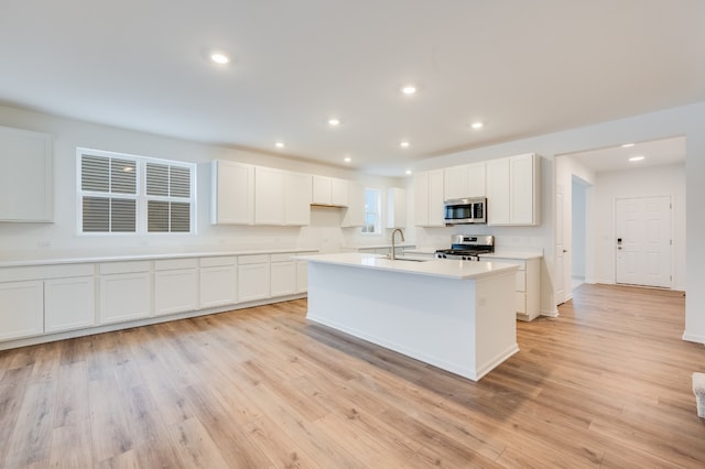 kitchen with stainless steel appliances, white cabinetry, sink, and a center island with sink