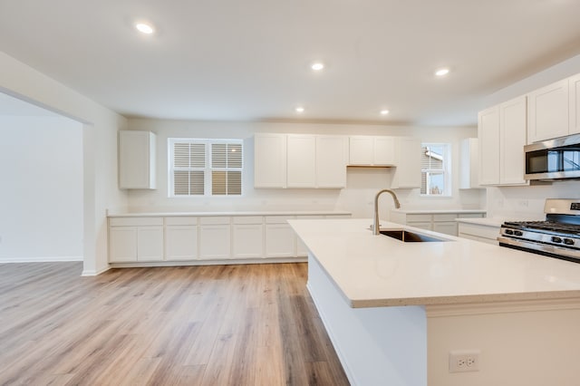 kitchen with a kitchen island with sink, sink, white cabinets, and appliances with stainless steel finishes