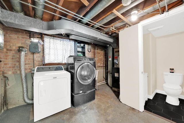 clothes washing area with washer and clothes dryer and brick wall