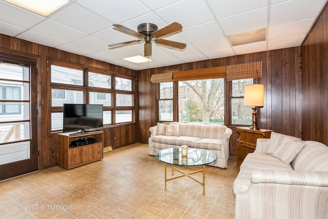 living room featuring wooden walls, ceiling fan, and a paneled ceiling