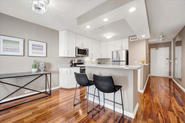 kitchen featuring dark hardwood / wood-style floors, white cabinets, a center island, light stone counters, and stainless steel appliances