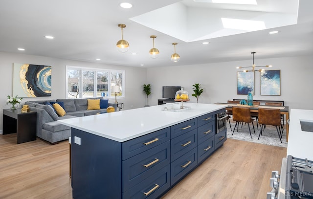 kitchen with a skylight, blue cabinets, hanging light fixtures, a center island, and light hardwood / wood-style floors