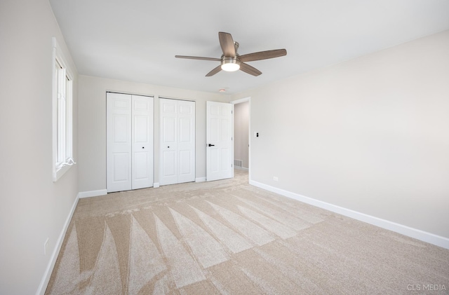 unfurnished bedroom featuring two closets, light colored carpet, and ceiling fan