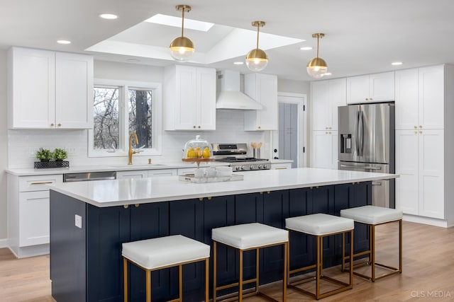 kitchen featuring appliances with stainless steel finishes, white cabinetry, sink, a center island, and wall chimney range hood