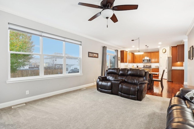 carpeted living room featuring crown molding, a healthy amount of sunlight, and ceiling fan