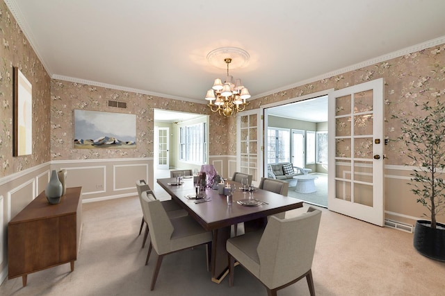 carpeted dining space with ornamental molding, a chandelier, and french doors