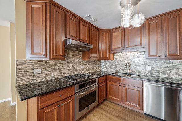 kitchen with appliances with stainless steel finishes, decorative light fixtures, tasteful backsplash, sink, and light hardwood / wood-style floors