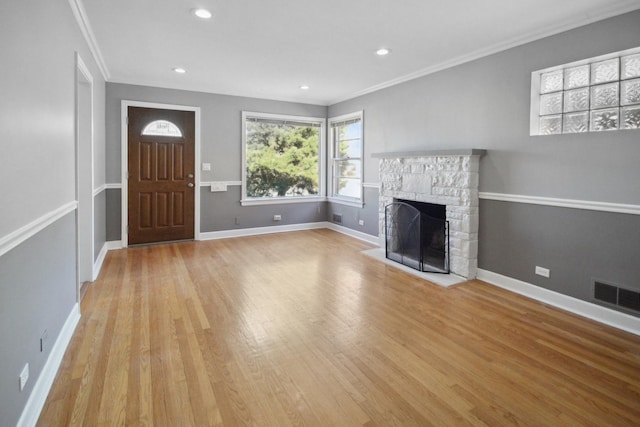 unfurnished living room featuring ornamental molding, a stone fireplace, and light hardwood / wood-style flooring