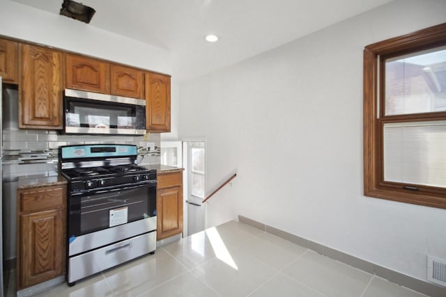 kitchen featuring stainless steel appliances, light tile patterned flooring, backsplash, and light stone counters