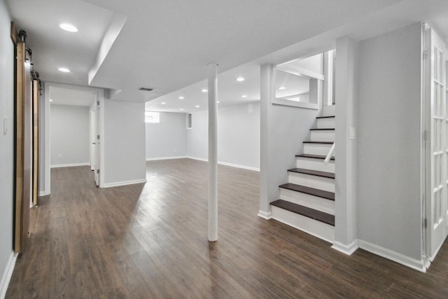 basement with a barn door and dark wood-type flooring