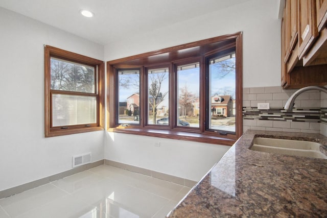 kitchen with dark stone countertops, sink, backsplash, and light tile patterned floors