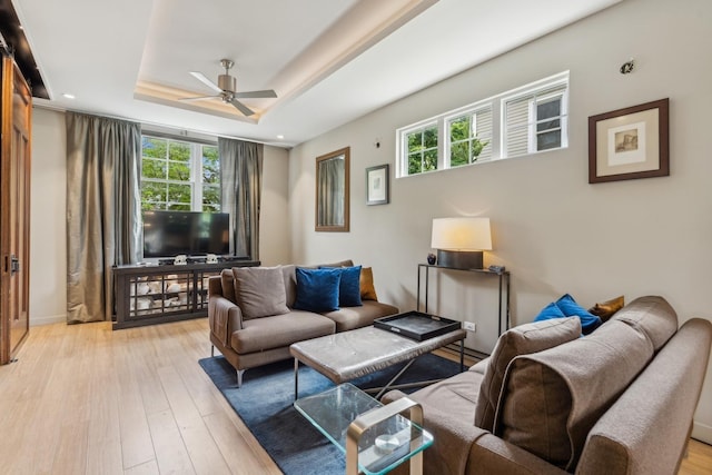 living room with a raised ceiling, ceiling fan, and light hardwood / wood-style floors