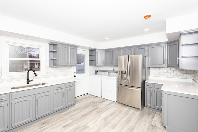 kitchen with stainless steel refrigerator with ice dispenser, sink, washer and dryer, gray cabinets, and backsplash