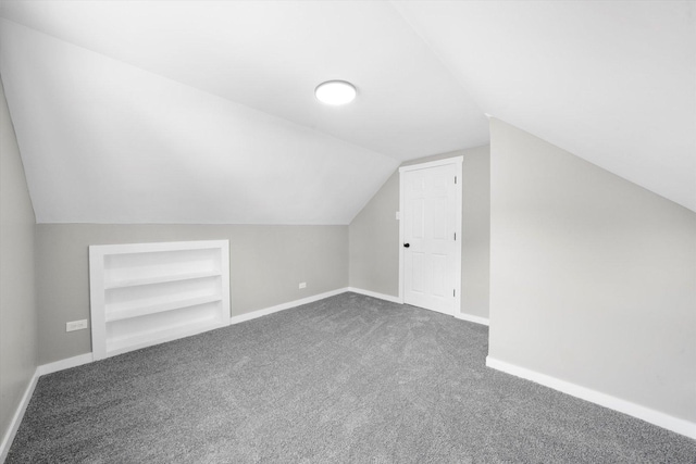 bonus room featuring vaulted ceiling, built in features, and dark colored carpet