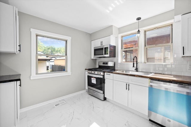 kitchen with pendant lighting, sink, backsplash, stainless steel appliances, and white cabinets