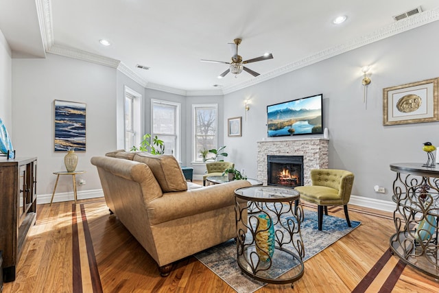 living room featuring hardwood / wood-style flooring, crown molding, ceiling fan, and a fireplace