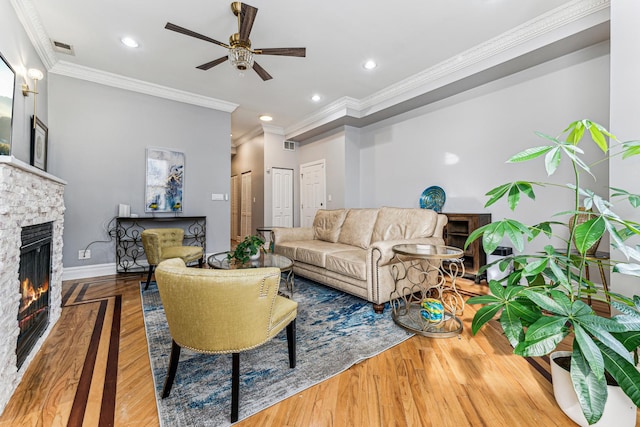 living room featuring hardwood / wood-style flooring, ornamental molding, a stone fireplace, and ceiling fan