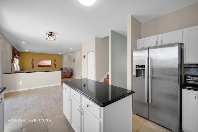 kitchen with light tile patterned flooring, dark stone countertops, white cabinets, a center island, and stainless steel refrigerator with ice dispenser