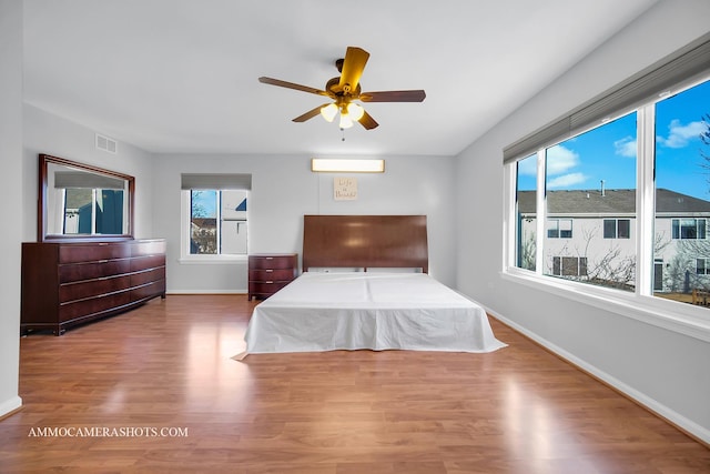 bedroom featuring hardwood / wood-style flooring, a wall mounted air conditioner, and ceiling fan