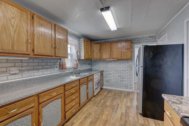 kitchen with sink, stainless steel fridge, dishwasher, brick wall, and light hardwood / wood-style floors