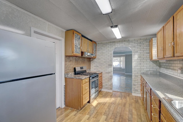 kitchen featuring sink, light stone counters, stainless steel appliances, light hardwood / wood-style floors, and backsplash