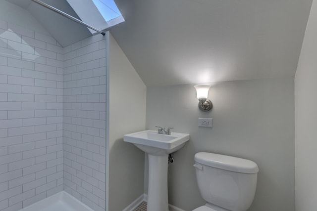 bathroom with a tile shower, lofted ceiling with skylight, and toilet