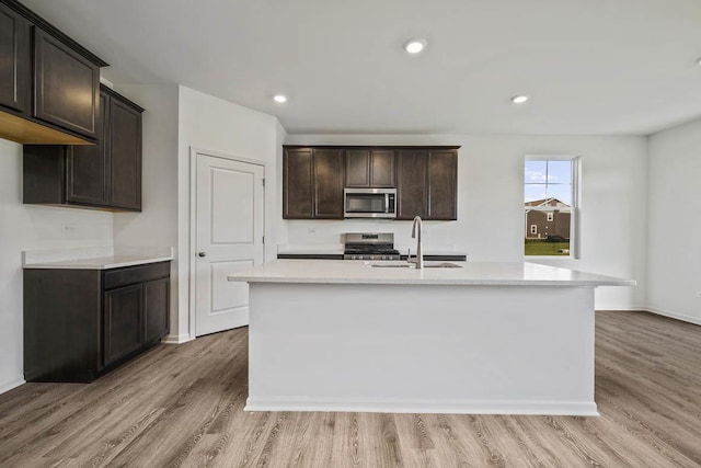 kitchen with dark brown cabinetry, stainless steel appliances, sink, and an island with sink