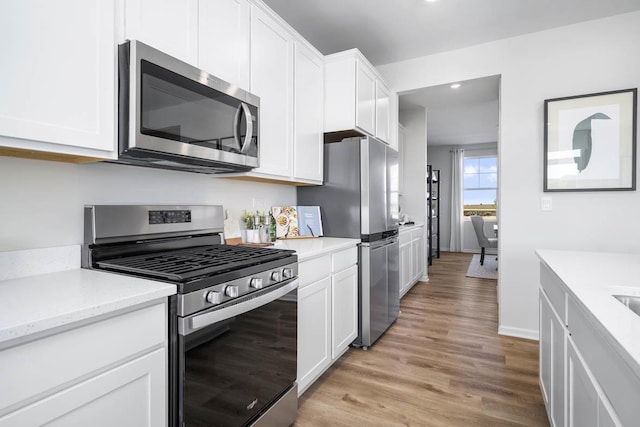 kitchen with light stone countertops, white cabinetry, appliances with stainless steel finishes, and light wood-type flooring