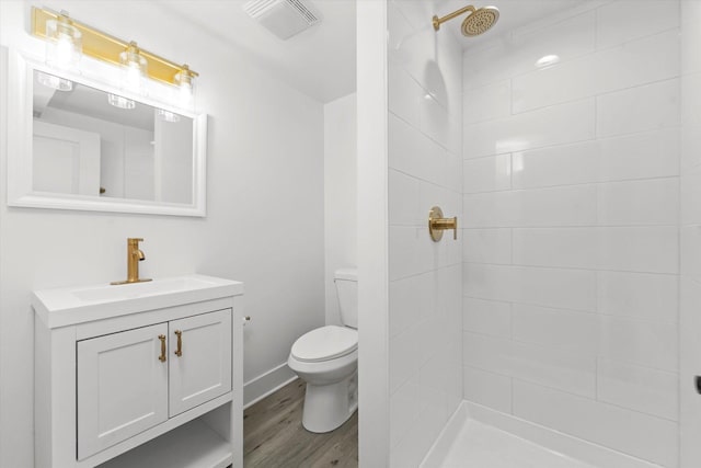 bathroom with hardwood / wood-style floors, vanity, a tile shower, and toilet