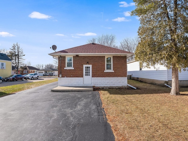 view of front of property featuring roof with shingles, a front yard, and brick siding