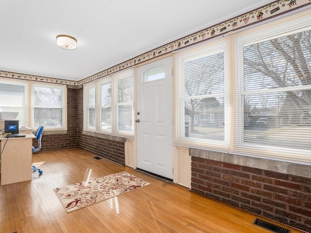 unfurnished office featuring visible vents, brick wall, and hardwood / wood-style flooring