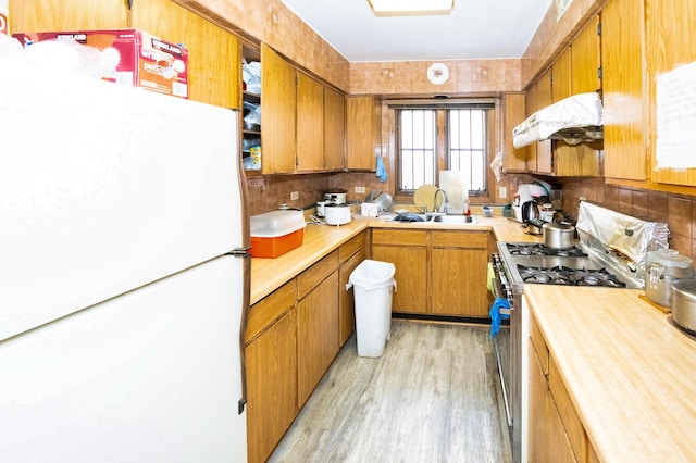 kitchen featuring white refrigerator, sink, light hardwood / wood-style flooring, and stainless steel gas stove