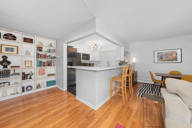 kitchen featuring appliances with stainless steel finishes, white cabinetry, a kitchen bar, light hardwood / wood-style floors, and kitchen peninsula