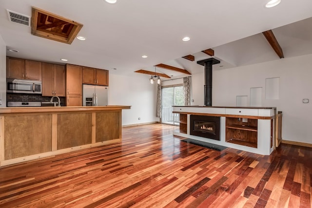 kitchen featuring sink, hardwood / wood-style flooring, appliances with stainless steel finishes, tasteful backsplash, and beamed ceiling