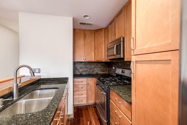 kitchen with appliances with stainless steel finishes, sink, dark stone countertops, and dark wood-type flooring