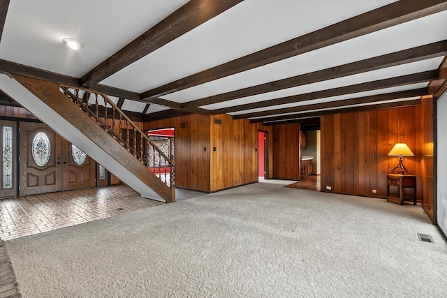 unfurnished living room featuring light carpet, beamed ceiling, and wood walls