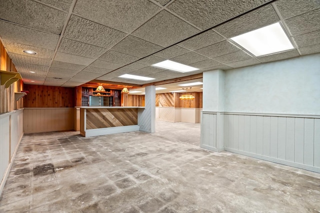 basement featuring a paneled ceiling, wooden walls, and indoor bar