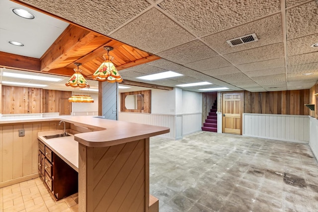 kitchen with wooden walls, a paneled ceiling, decorative light fixtures, and sink