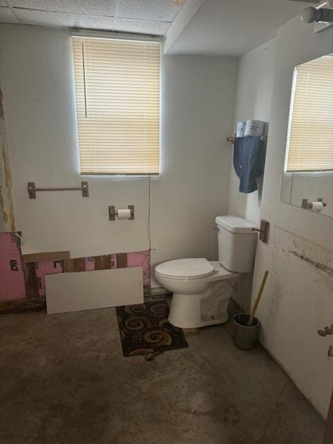 bathroom with a paneled ceiling, toilet, and concrete floors
