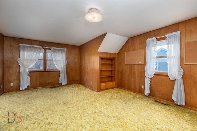 additional living space with plenty of natural light, light carpet, built in features, and wooden walls