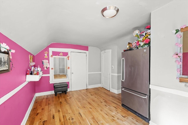 kitchen with vaulted ceiling, stainless steel refrigerator, and wood-type flooring