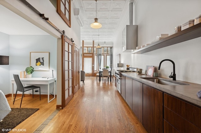 interior space featuring dark brown cabinetry, wall chimney exhaust hood, sink, a barn door, and high end stove