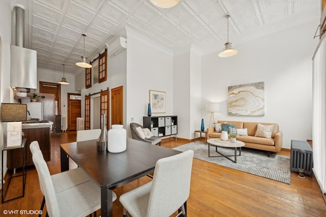 dining area with wood-type flooring, a barn door, radiator heating unit, and a high ceiling