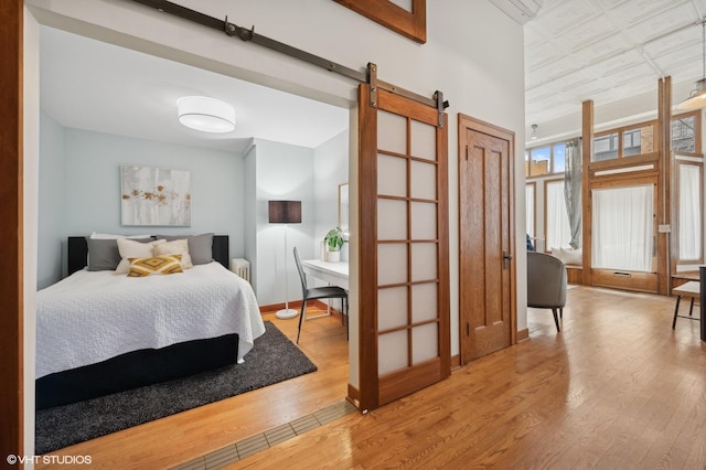 bedroom featuring a high ceiling, a barn door, and light hardwood / wood-style flooring