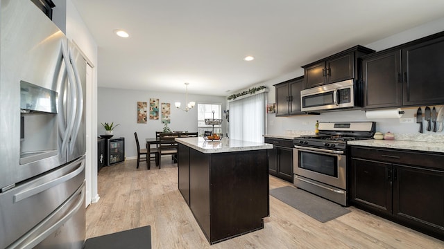 kitchen with an inviting chandelier, hanging light fixtures, stainless steel appliances, a center island, and light hardwood / wood-style floors