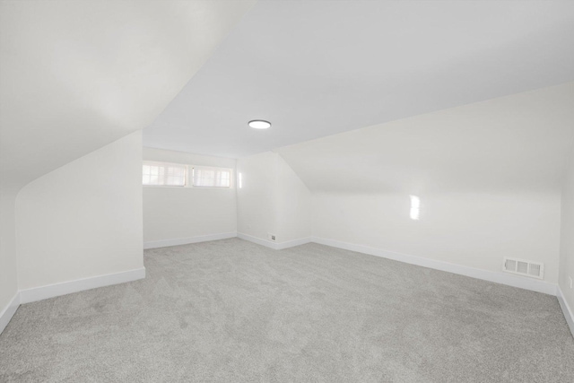 additional living space featuring vaulted ceiling and light carpet