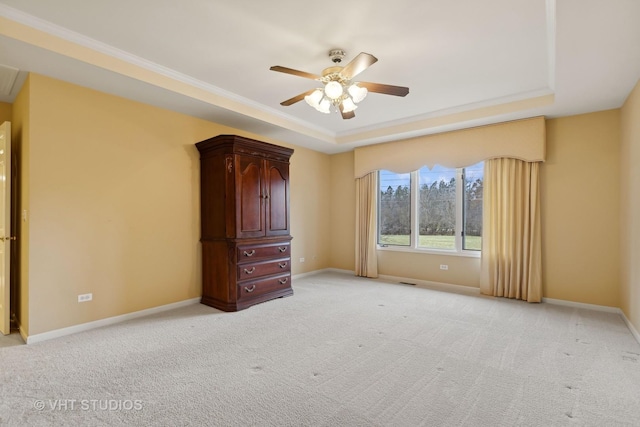 unfurnished bedroom featuring crown molding, a tray ceiling, light colored carpet, and ceiling fan